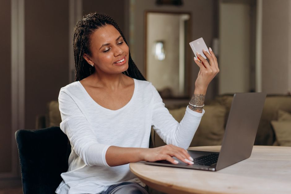 African American woman happily shopping online with her laptop and credit card at home.